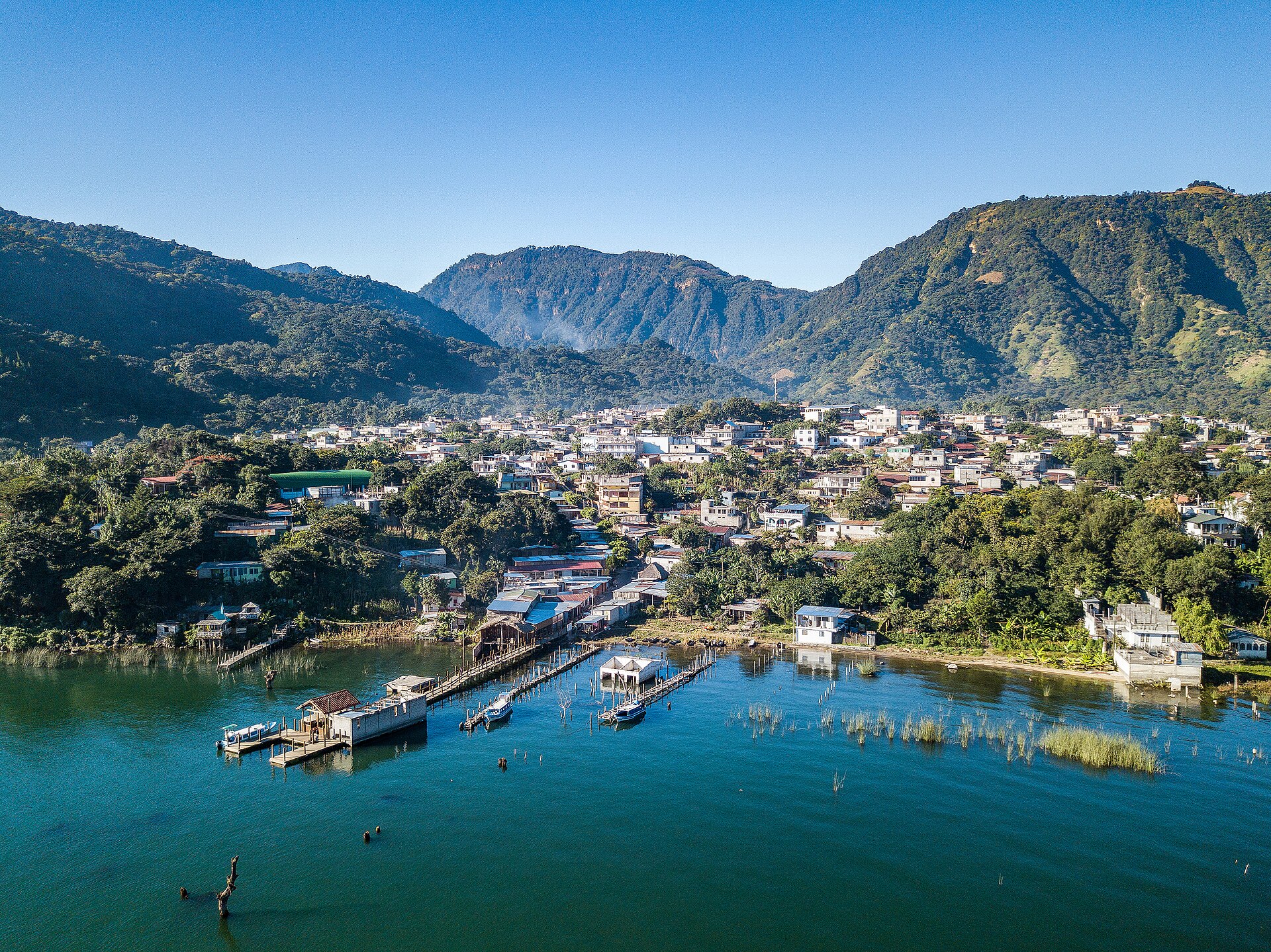 An aerial view of San Juan La Laguna between green hills and Lake Atitlán