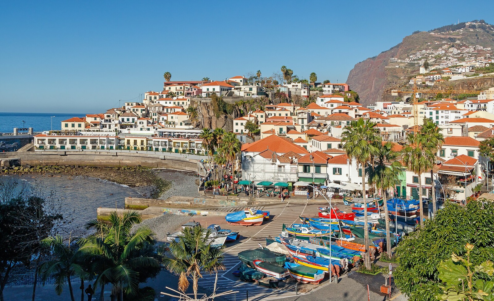 Colorful fishing boats beside the bay and red-roofed houses of Câmara de Lobos.